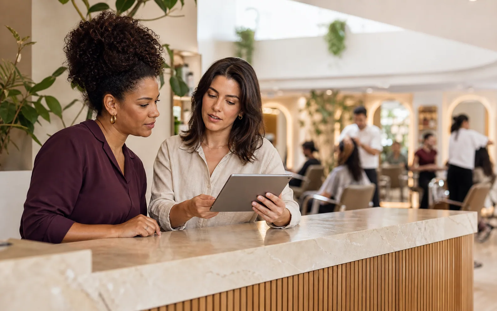 Dona de salão e recepcionista revisando a agenda juntas em um tablet